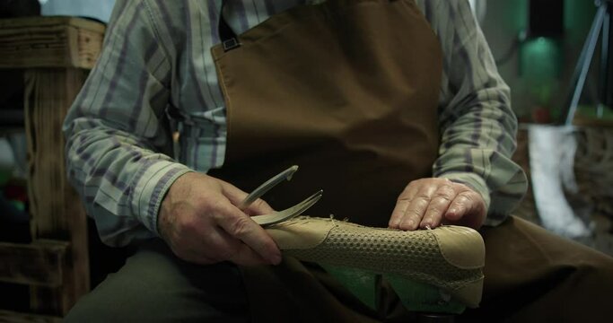 Mature bootmaker take out nails from a shoe upper at the private workshop. 