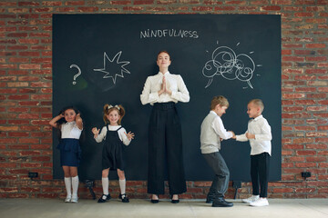 Mindfulness. Young woman in formal wear standing by blackboard with little children. Education,...