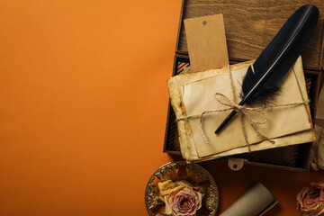 Wooden box with old letters and feather on orange background, space for text