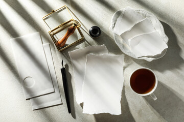 Sheets of paper, stamp, ink bottle and pen, cup of tea on light background, top view