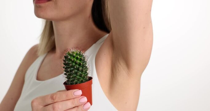 Young woman in white shirt with raised hand brings miniature cactus in pot to armpit. Lady with impulsive pain in armpit. Acute chronic health problems concept