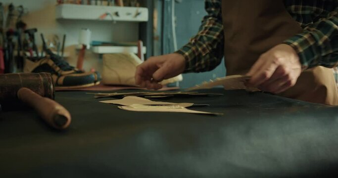 Young male bootmaker putting patterns on table for new project at the workshop.