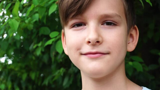 a ten-year-old boy looks into the camera against the background of green leaves of a bush.
