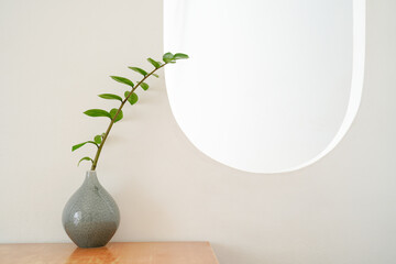 A branch of green leaves in a grey ceramic vase on white background