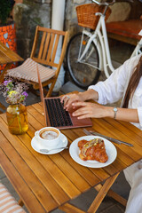 In a summer cafe, a woman surfs the net on a laptop while eating a croissant