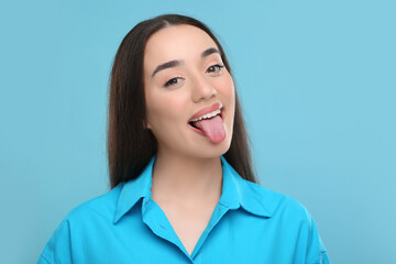 Happy woman showing her tongue on light blue background