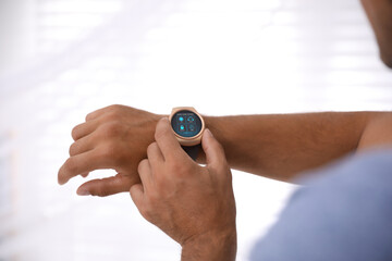 Man setting smart home control system via smartwatch against light background, closeup. App...