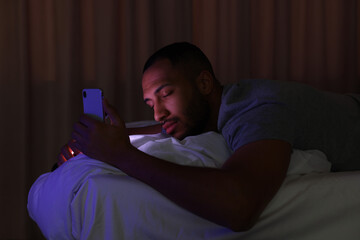 Fototapeta premium Young man sleeping while holding smartphone in bed at night. Internet addiction