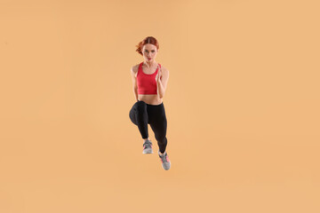 Fototapeta na wymiar Young woman in sportswear jumping on beige background