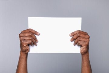 African American man holding sheet of paper on grey background, closeup. Mockup for design