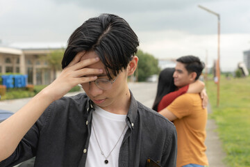 A young asian man sulks and walks away from his ex-girlfriend being comforted by another man. An ex-partner saddened after being replaced and dumped. - obrazy, fototapety, plakaty