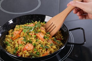 Woman cooking tasty rice with shrimps and vegetables on induction stove, closeup