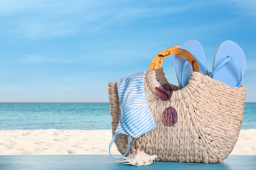 Bag with bikini and accessories on sunny ocean beach, space for text. Summer vacation