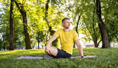 Man doing morning yoga at park outdoors in summer time. Guy stretching his back at nature in sunny day