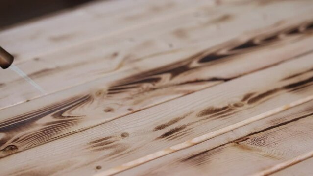  Tip of a propane torch moves over a pine board burning in the grain