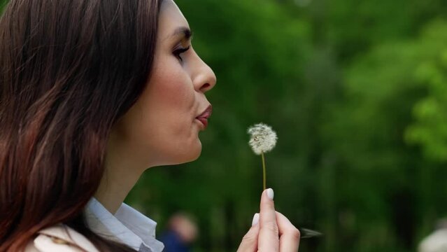 Young girl blows a dandelion and smiles. the concept of happiness, a happy moment, joyful moments. Close up. Middle of the park in big city