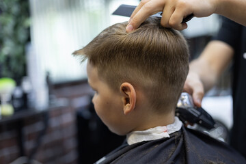A child in a hairdresser does a hairstyle. The child sits quietly in the chair while the hairdresser works with scissors The hairdresser works in a hairdressing salon to make a hairstyle for a child.