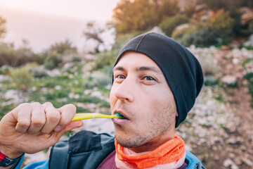 a male hiker in hat brushes his teeth at a camping site. Hygiene and dental health in the woods
