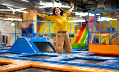 Pretty girl jumping on colorful trampoline at playground park and smiling. Beautiful young woman...