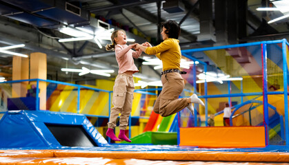 Pretty girl and her daughter kid jumping on colorful trampoline at playground park and smiling. Caucasian family happy during active entertaiments - obrazy, fototapety, plakaty