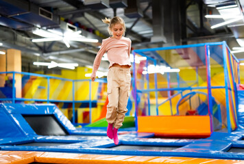 Pretty girl kid jumping on colorful trampoline at playground park and smiling. Caucasian preteen...