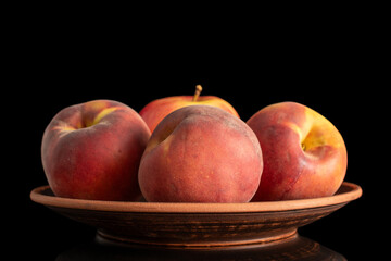 Three organic peaches and one apple on a clay dish, macro, isolated on black background.