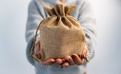 Person holding burlap bag in hands with gift inside. Girl with rustic beige pouch packaging made with organic textile