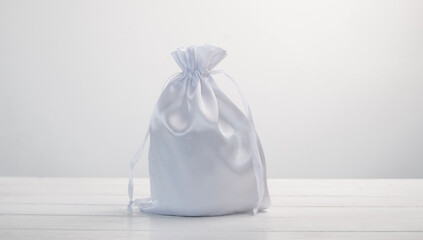 White gift bag made with silk material on white background. Stylish soft pouch with present inside