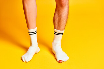 Male and female legs standing in white socks against bright yellow studio background. Hairy and smooth legs. Concept of creativity, imagination and inspiration, fashion, ad. Pop art