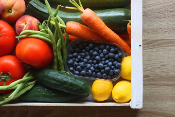 Wooden crate full of healthy seasonal fruit and vegetable. Top view, wooden background.