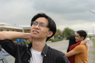 A young asian man trying to figure out what went wrong after being left by his ex-girlfriend for another man. An ex-partner saddened after being replaced and dumped. - obrazy, fototapety, plakaty
