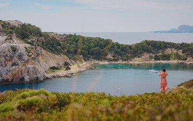 Fototapeta premium Asian woman in hat look on views of azure Bay in Mediterranean sea. Travel and vacation concept. Anthony Quinn bay with crystal clear water in Rhodes island, Greece. The most beautiful beach.