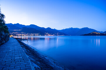 Il paese di Pianello del lario, sul lago di Como, e la passeggiata lungo il lago, all'imbrunire. Alpi, montagne e paesi del lago in lontananza.