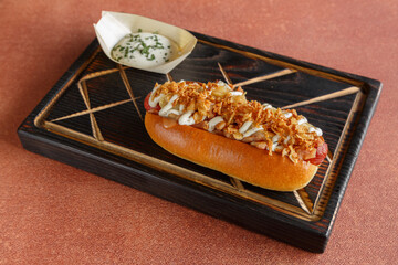 Hot-dog avec saucisse, ketchup, moutarde sur une planche en bois et fond orange.