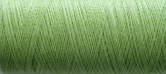 Green sewing thread in spool for sew hobby closeup. Macro bobbin view for needlework
