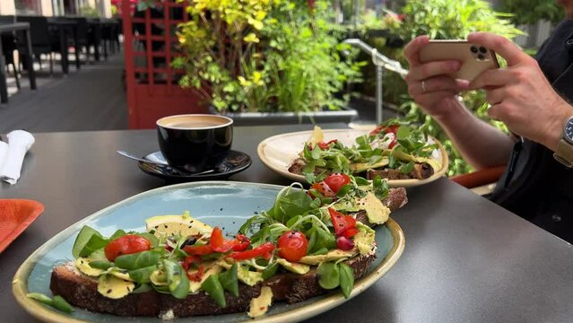 Avocado toasts being shot with smartphone in male hands in street cafe