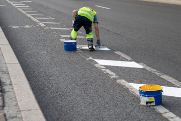 Man road worker applies markings on asphalt road separating bike path from carriageway for cars in city. Create comfortable urban infrastructure for safe road traffic. Bike lane for bicycles in town. - obrazy, fototapety, plakaty