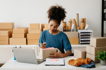 Fototapeta na wymiar Young African business owner woman prepare parcel box and standing check online orders for deliver to customer on tablet, laptop Shopping Online concept. in office