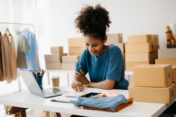 Fototapeta na wymiar Young African business owner woman prepare parcel box and standing check online orders for deliver to customer on tablet, laptop Shopping Online concept. in office