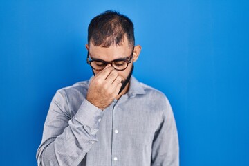 Middle east man with beard standing over blue background tired rubbing nose and eyes feeling fatigue and headache. stress and frustration concept.