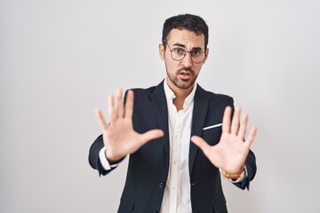 Handsome business hispanic man standing over white background afraid and terrified with fear expression stop gesture with hands, shouting in shock. panic concept.