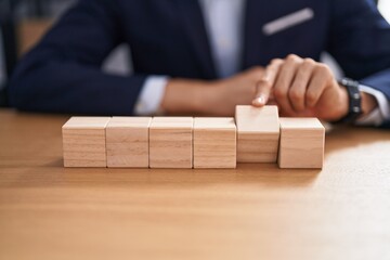 Young blond man business worker sitting on table with wooden cubes at office