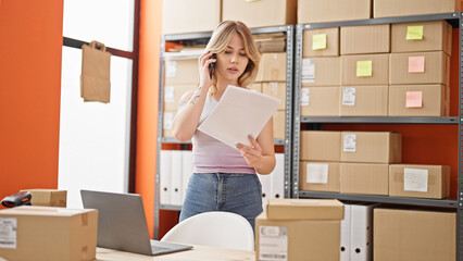 Young blonde woman ecommerce business worker talking on smartphone reading document at office