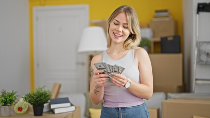 Young blonde woman smiling confident holding money at new home