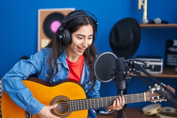 Fototapeta na wymiar Young hispanic girl musician singing song playing classical guitar at music studio
