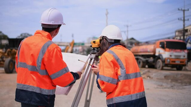 Surveyor engineers wearing safety uniform ,helmet and radio communication with equipment theodolite to measurement positioning on the construction site of the road with construct machinery background.