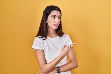Young beautiful woman standing over yellow background pointing aside worried and nervous with...
