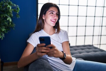 Young beautiful hispanic woman using smartphone sitting on sofa at home