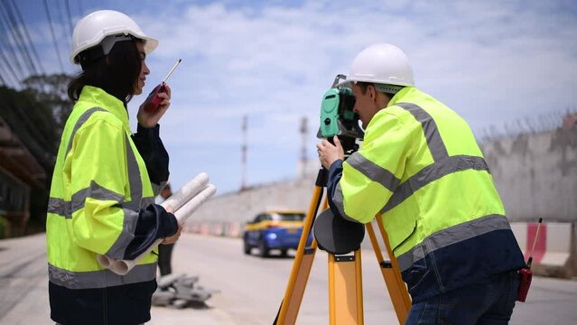 Surveyor engineers wearing safety uniform ,helmet and radio communication with equipment theodolite to measurement positioning on the construction site of the road with construct machinery background.