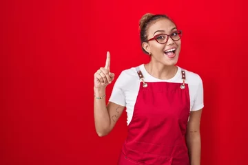 Zelfklevend Fotobehang Young hispanic woman wearing waitress apron over red background pointing finger up with successful idea. exited and happy. number one. © Krakenimages.com